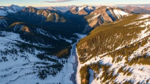 Aerial view of Colorado mountain snowpack in spring with alpine lakes and evergreen forests, sunlit peaks with melting snow flowing into watershed valleys