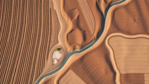 Aerial view of agricultural fields with visible soil erosion patterns and water runoff channels cutting through brown earth, showing the contrast between cultivated rows and natural landscape features